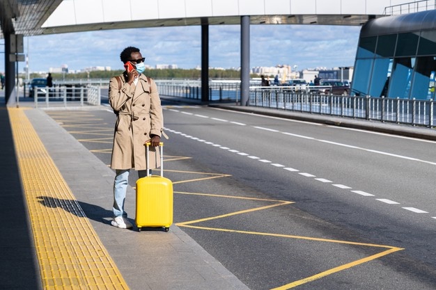 afro-traveler-man-stands-airport-terminal-calling-mobile-waiting-taxi-wear-face-mask_165285-1998